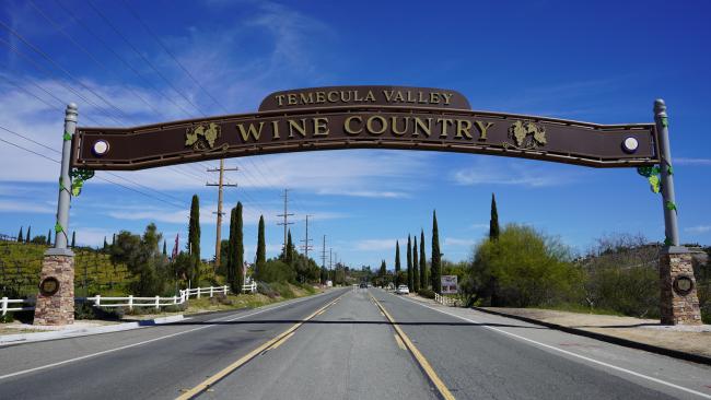A street level view on Rancho California Road in Temecula under a the new Wine Country Archway which spans 75 feet across the road. The arch says Temecula Valley Wine Country and has grape motifs along the arch.
