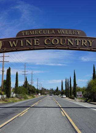 A street level view on Rancho California Road in Temecula under a the new Wine Country Archway which spans 75 feet across the road. The arch says Temecula Valley Wine Country and has grape motifs along the arch.